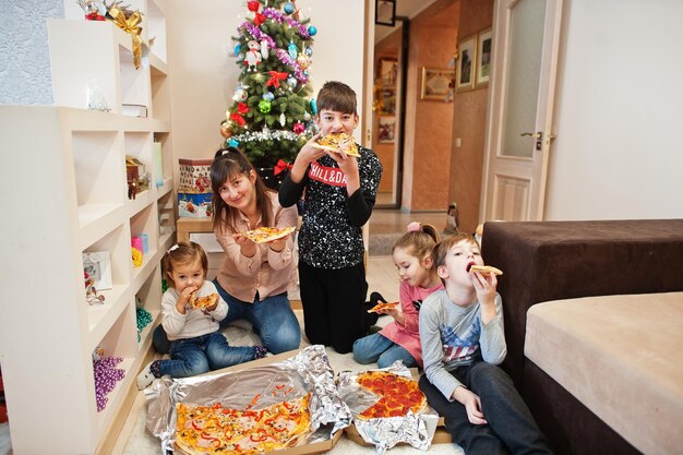 Famiglia felice con quattro bambini che mangiano pizza a casa.