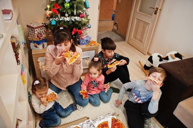 Famiglia felice con quattro bambini che mangiano pizza a casa.