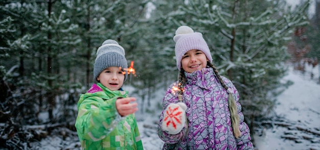 Famiglia felice con stelle filanti in fiamme durante la camminata nella foresta il giorno della nevicata celebrazione di natale