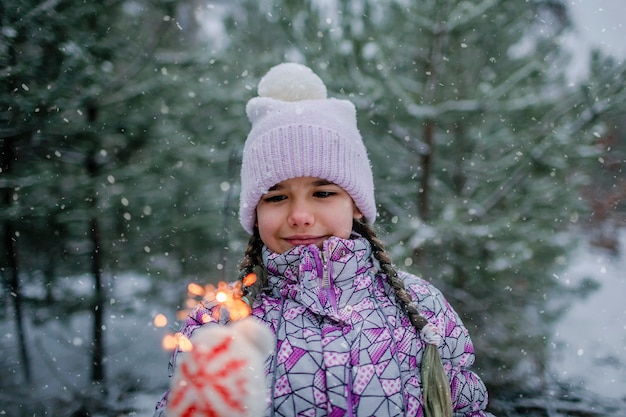 Famiglia felice con stelle filanti in fiamme durante la camminata nella foresta il giorno della nevicata celebrazione di natale