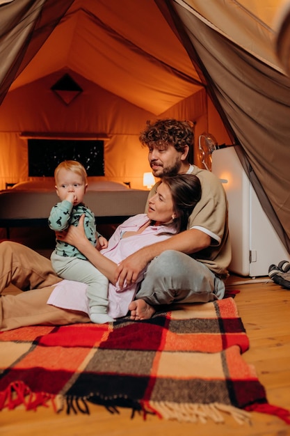 Famiglia felice con un bambino adorabile che gioca e trascorre del tempo insieme in glamping la sera d'estate Tenda da campeggio di lusso per attività ricreative e ricreative all'aperto Concetto di stile di vita