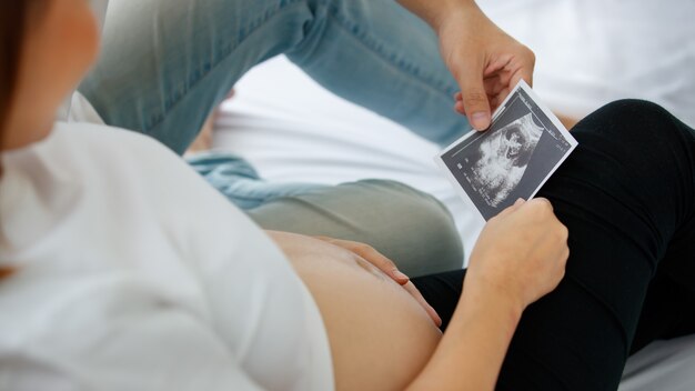Famiglia felice, concetto di bambino sano. Foto di una mano di un uomo e di una donna che tengono e guardano la foto dell'ecografia del loro feto. Messa a fuoco selettiva su una foto di scansione.