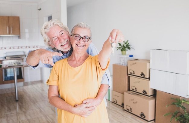 Famiglia felice coppia di persone anziane che tengono le chiavi della nuova casa per un nuovo inizio come in pensione con scatole in movimento sul pavimento