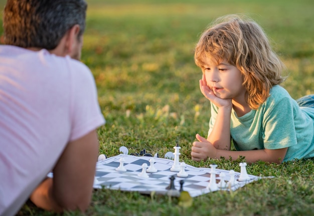 Famiglia felice di genitore e figlio che giocano a scacchi sull'erba verde nello sviluppo dell'infanzia all'aperto del parco
