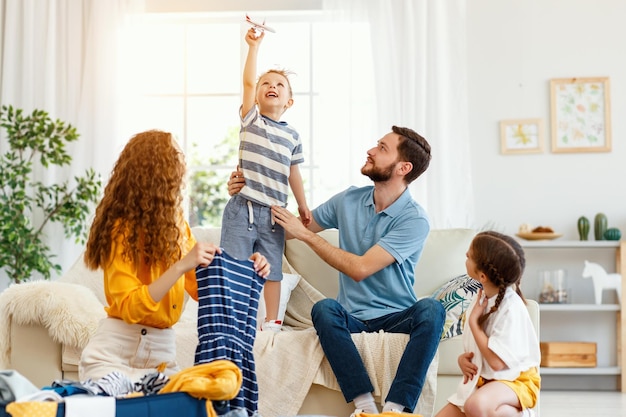 Famiglia felice di genitori e ragazzo con una ragazza che fa le valigie per il viaggio di vacanza mentre gioca sul divano in soggiorno