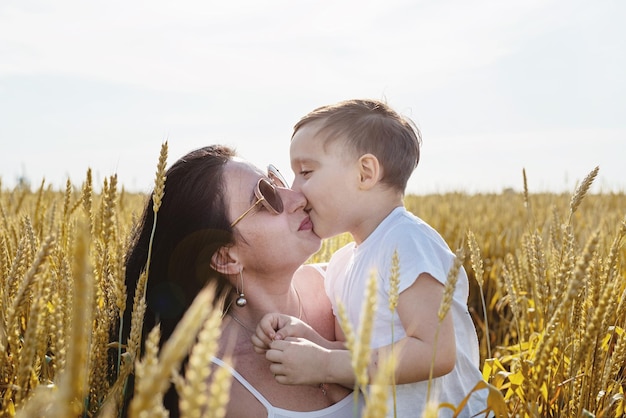 Famiglia felice di madre e bambino che cammina sul campo di grano baciando