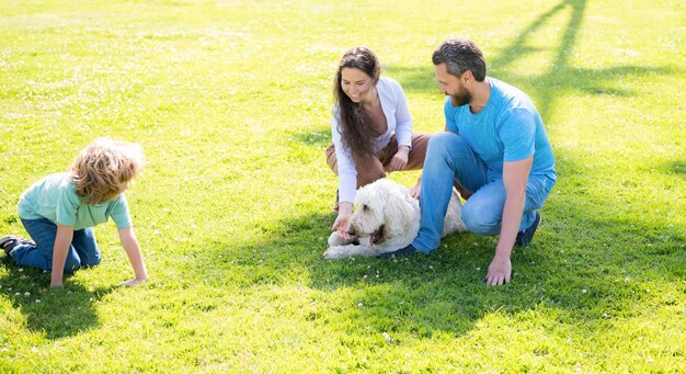 Famiglia felice di mamma padre e figlio del bambino che giocano con il cane negli amanti dei cani di erba verde parco estivo