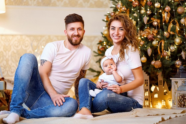 Famiglia felice di mamma papà e piccola bambina seduta vicino all'albero di Natale sul pavimento