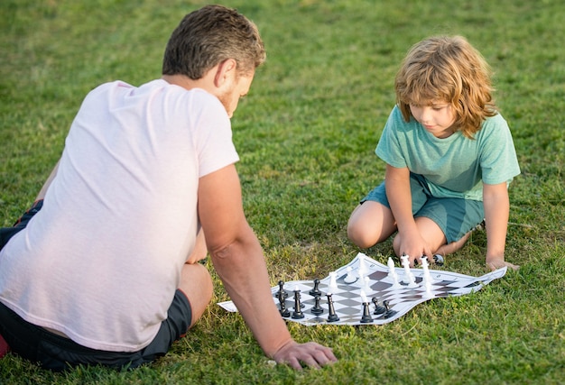 Famiglia felice di padre e figlio che giocano a scacchi sull'erba verde nel parco all'aperto, avversario.