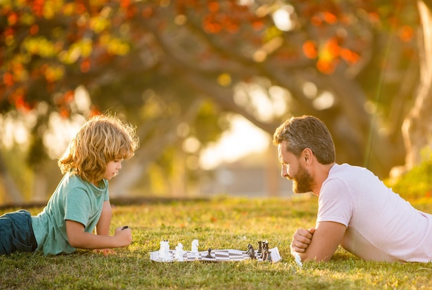 Famiglia felice di papà e figlio che giocano a scacchi sull'erba verde nel parco a scacchi all'aperto