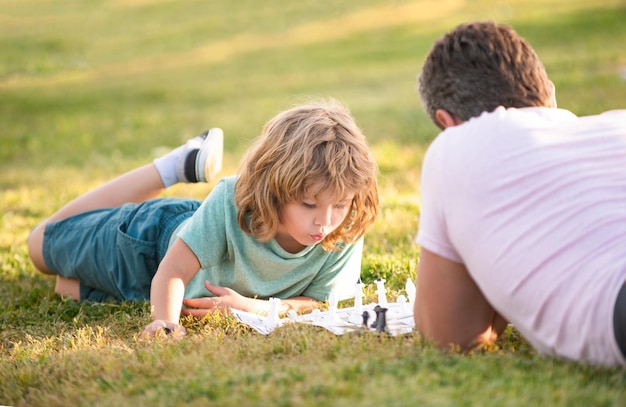 Famiglia felice di papà e figlio che giocano a scacchi sull'erba verde nel parco strategico all'aperto