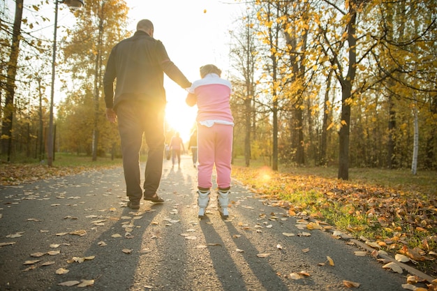 Famiglia felice di papà e sua figlia che camminano nel parco la ragazza che cavalca sui rulli