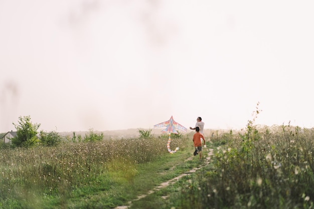 Famiglia felice e bambini corrono sul prato con un aquilone in estate sulla natura Famiglia che gioca con l'aquilone mentre corre lungo il campo estivo rurale Giornata della famiglia
