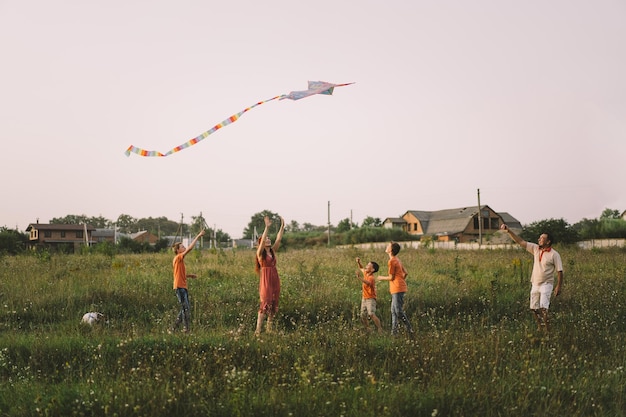 Famiglia felice e bambini corrono sul prato con un aquilone in estate sulla natura Famiglia che gioca con l'aquilone mentre corre lungo il campo estivo rurale Giornata della famiglia