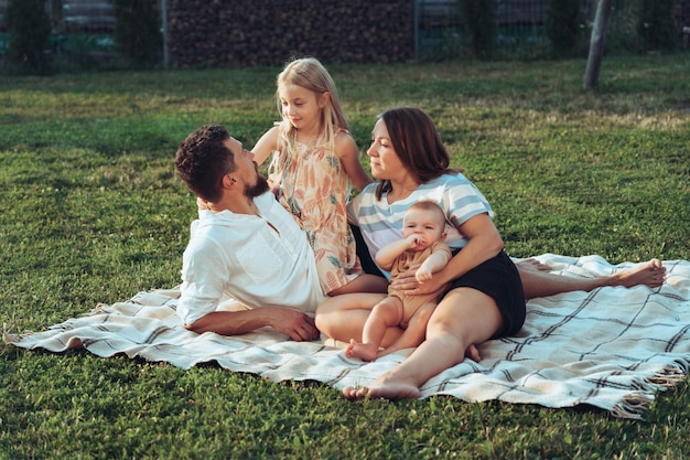 Famiglia felice e bambini piccoli che si divertono insieme riposando su una coperta in estate