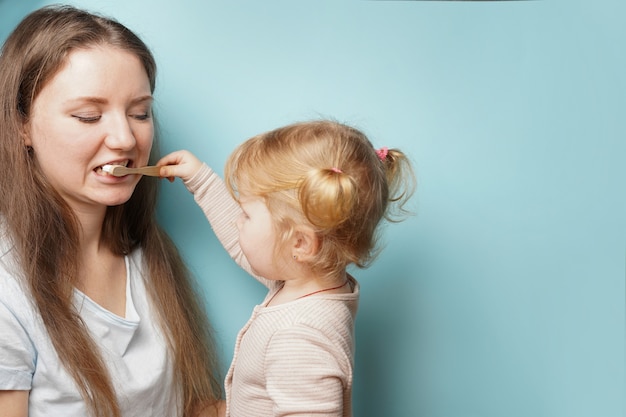 Famiglia felice e salute. madre e figlia bambino ragazza lavarsi i denti insieme sulla superficie blu