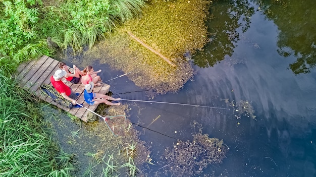 Famiglia felice ed amici che pescano insieme all'aperto vicino al lago di estate, vista superiore aerea da sopra