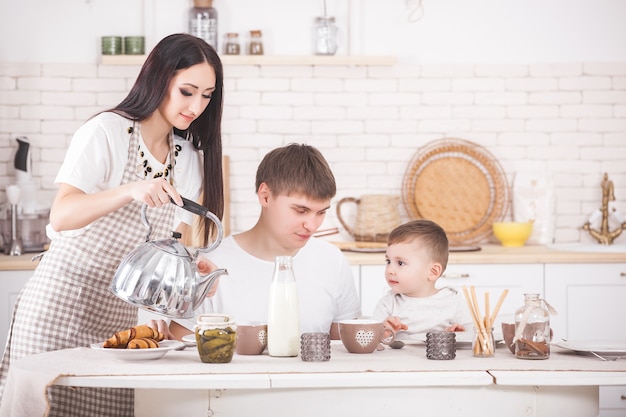 Famiglia felice facendo colazione insieme. Giovane famiglia che mangia al tavolo sulla cucina. Mamma, papà e bambino piccolo mangiano.