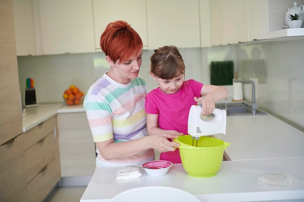 Famiglia felice in cucina che gioca e impara a cucinare rimanendo a casa durante l'isolamento pandemico del coronavirus covid-19. Figlia del bambino e della madre che prepara la torta ed i biscotti