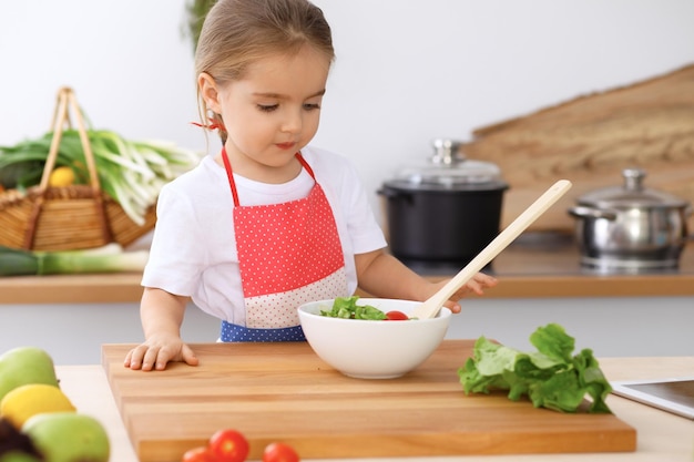 Famiglia felice in cucina Madre e figlia che cucinano gustosa colazione a base di insalata fresca Piccolo aiutante che affetta e mescola pomodori e verde