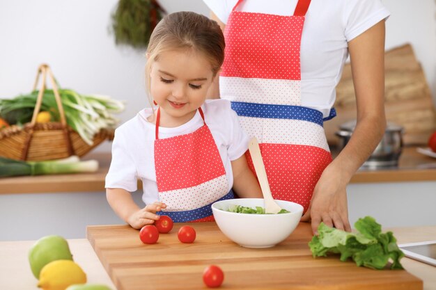 Famiglia felice in cucina Madre e figlia che cucinano gustosa colazione a base di insalata fresca Piccolo aiutante che affetta e mescola pomodori e verde