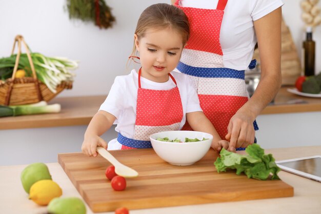 Famiglia felice in cucina Madre e figlia che cucinano gustosa colazione a base di insalata fresca Piccolo aiutante che affetta e mescola pomodori e verde