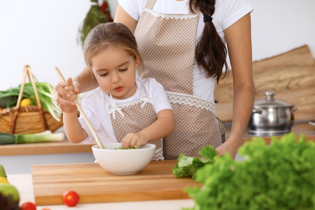 Famiglia felice in cucina Madre e figlia che cucinano gustosa colazione a base di insalata fresca Piccolo aiutante che affetta e mescola pomodori e verde