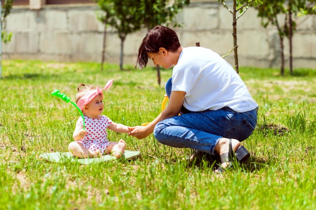 Famiglia felice in giardino. l'acqua da un annaffiatoio viene versata nelle mani del bambino. la madre si lava le mani a un bambino in giardino da un annaffiatoio giallo.