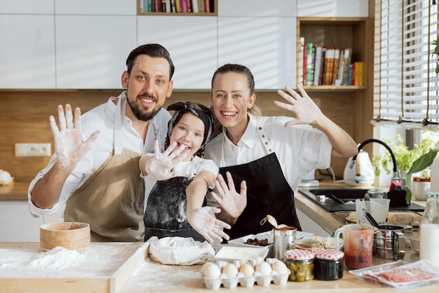 Famiglia felice in grembiuli che cucinano la cottura in cucina agitando mostrando le palme alla macchina fotografica