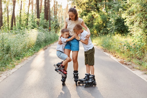 Famiglia felice in posa nel parco estivo, madre e due figli che pattinano insieme, donna che trascorre il fine settimana con i suoi figli in modo attivo, abbracciando i bambini e sorridendo felicemente.