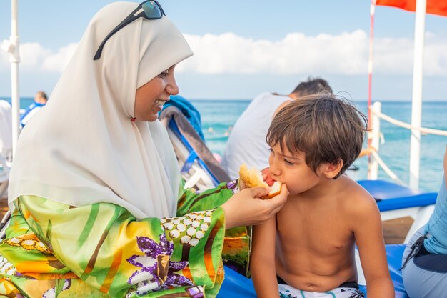 Famiglia felice in un picnic vicino al mare e la mamma che dà da mangiare a suo figlio