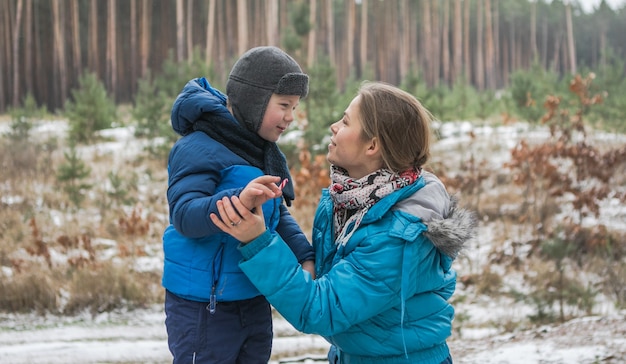 Famiglia felice in una passeggiata all'aperto nella soleggiata foresta invernale, vacanze di Natale, madre e figlio giocano insieme