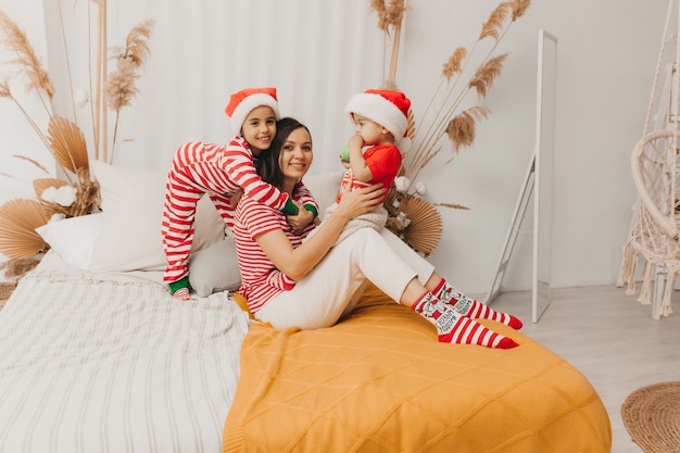 Famiglia felice, madre e bambini in pigiama e cappelli natalizi che si divertono a letto. Natale