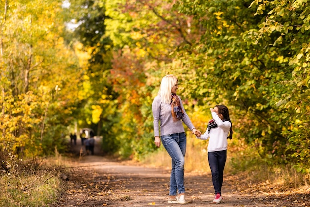 famiglia felice: madre e figlio piccola figlia giocano a coccolarsi durante la passeggiata autunnale nella natura all'aperto