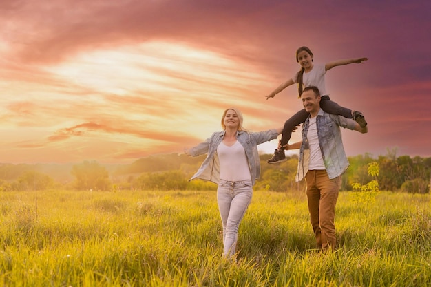 Famiglia felice: madre, padre, figlia sulla natura al tramonto.