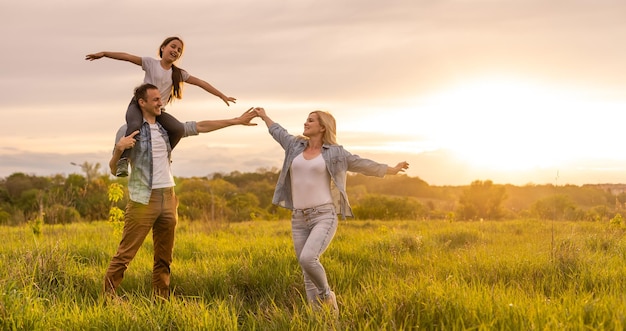 Famiglia felice: madre, padre, figlia sulla natura al tramonto.