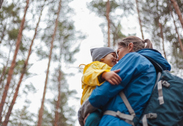 Famiglia felice Mamma e bambino camminano insieme nella foresta dopo la pioggia con gli impermeabili, si abbracciano e si guardano look