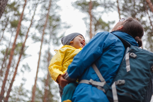 Famiglia felice Mamma e bambino camminano nella foresta dopo la pioggia in impermeabili insieme, si abbracciano e guardano il cielo