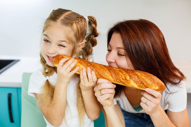 Famiglia felice, mamma e figlia mangiano un pane che morde da lati diversi. Rapporti familiari del bambino con i genitori