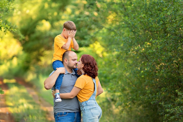 Famiglia felice, mamma, papà, figlio camminano, si abbracciano, si baciano per strada in estate