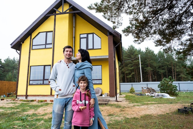 Famiglia felice nel cortile di una casa incompiuta acquisto di una costruzione di trasferimento di mutuo ipotecario cottage