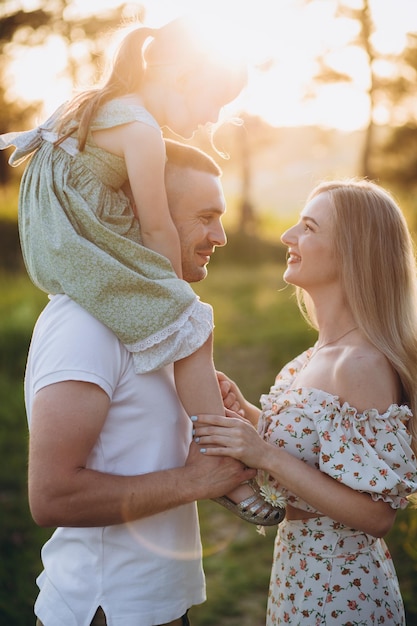 Famiglia felice nel parco la luce della sera Le luci di un sole Mamma papà e bambino camminano felici al tramonto Il concetto di una famiglia feliceI genitori tengono le mani del bambino