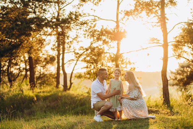 Famiglia felice nella luce della sera del parco Le luci di un sole Mamma papà e bambino camminano felici al tramonto Il concetto di una famiglia feliceI genitori tengono le mani del bambino