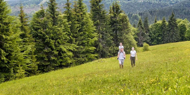 Famiglia felice: padre con figlio sulle spalle e madre vanno su un campo verde