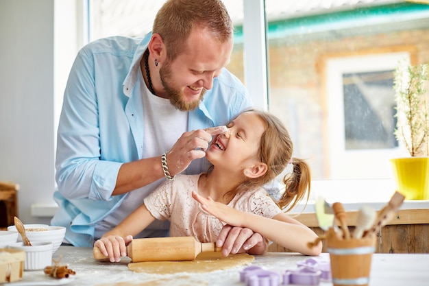 Famiglia felice, padre e figlia stendono la pasta per biscotti in una cucina a casa