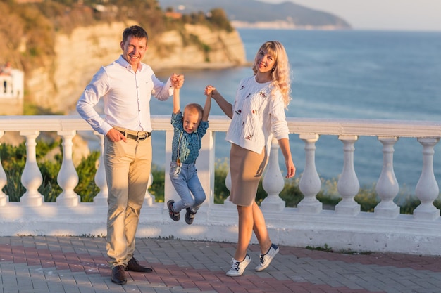 Famiglia felice padre madre bambino figlio cammina con divertimento lungo il bordo del mare al tramonto surf sul Mar Nero