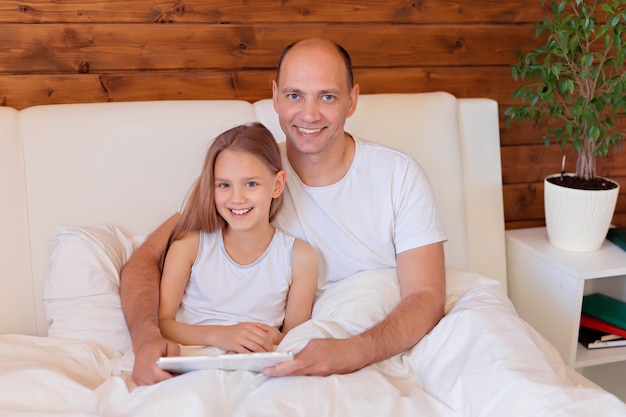 Famiglia felice, papà e figlia che parlano sul tablet a casa a letto. Insegnamento a distanza.