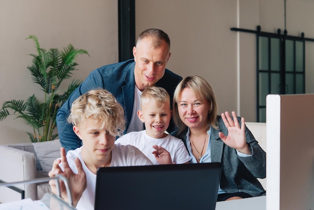 Famiglia felice, papà, mamma e due bambini, che agitano le mani durante una videochiamata tramite un laptop