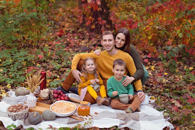 Famiglia felice, papà, mamma, figlio piccolo, figlia a un picnic autunnale con torta, zucca, tè