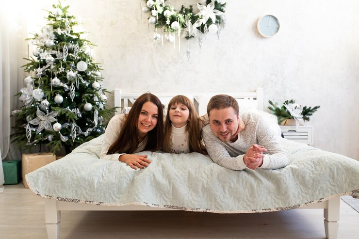 Famiglia felice sdraiata a letto vicino all'albero di Natale a casa